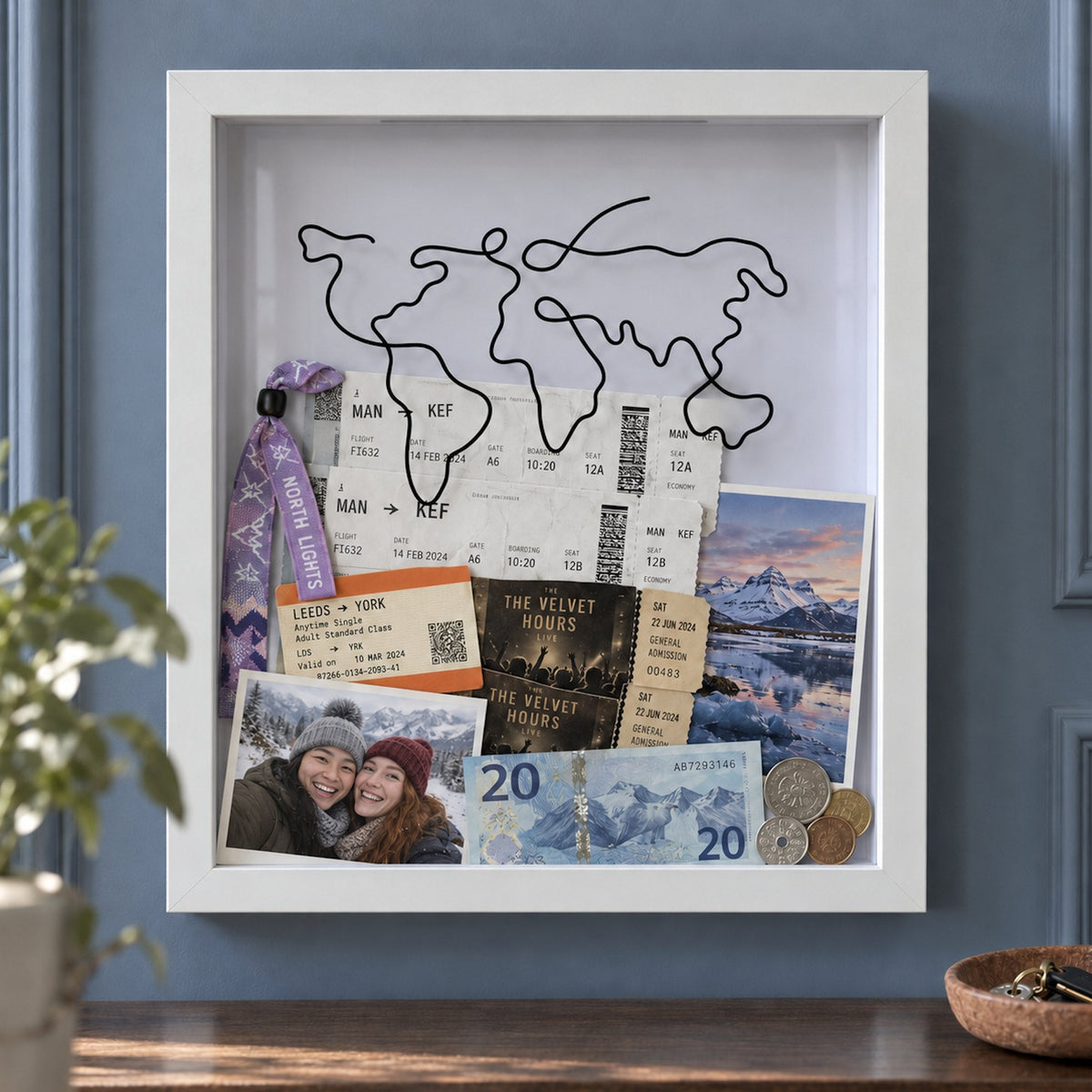 A northern lights wristband kept with Manchester to Keflavik boarding passes, a couple's photo in the snow and gig tickets inside a white Wandersake Memory Box on a blue panelled wall